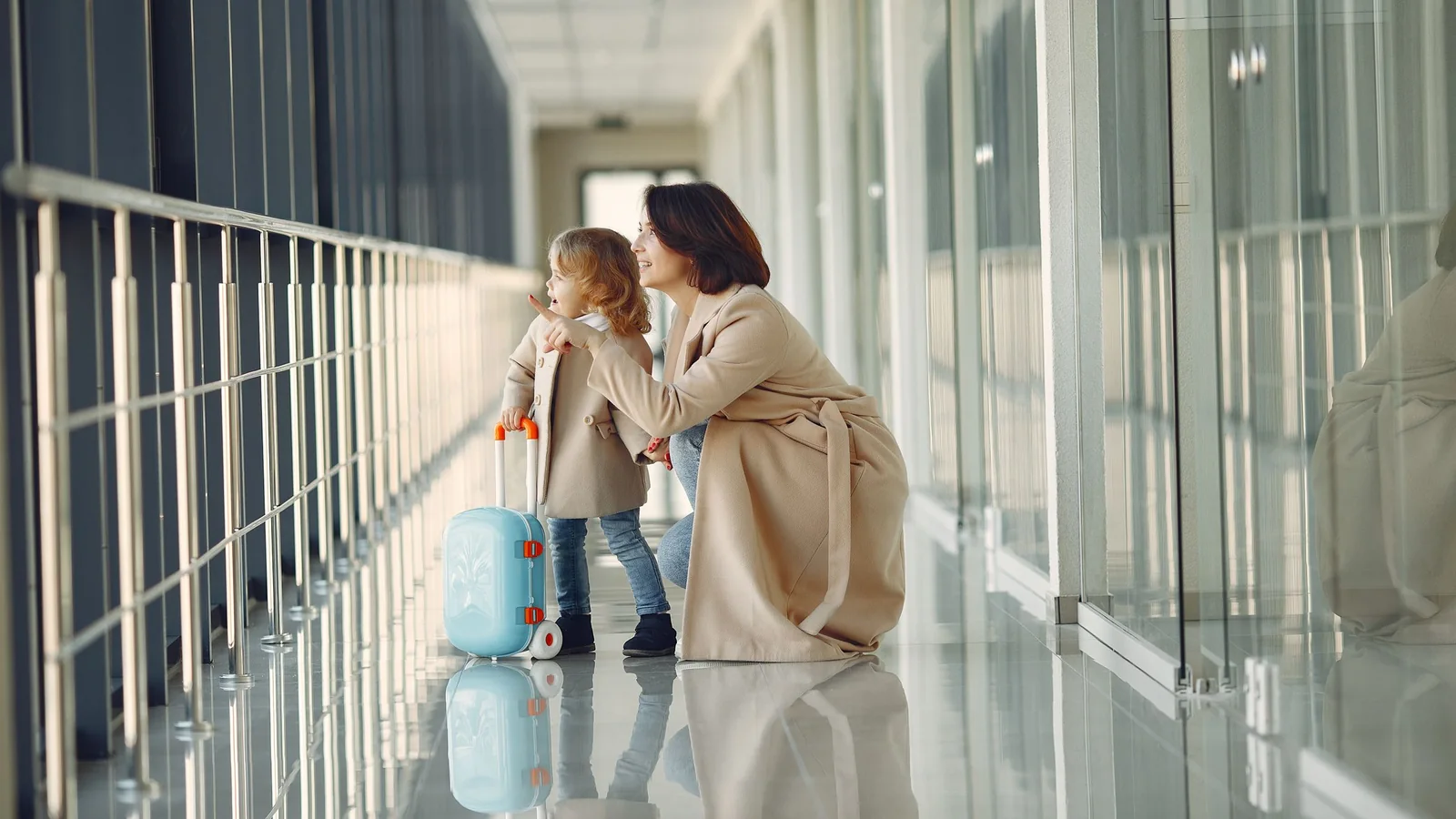 Mère et enfant regardant par la fenêtre – en famille et avec des bagages à l'aéroport de Dortmund