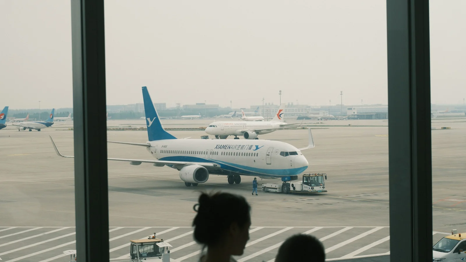 Eltern und Kind schauen durch die Terminalscheibe auf ein Flugzeug – mit Kindern am Flughafen Düsseldorf