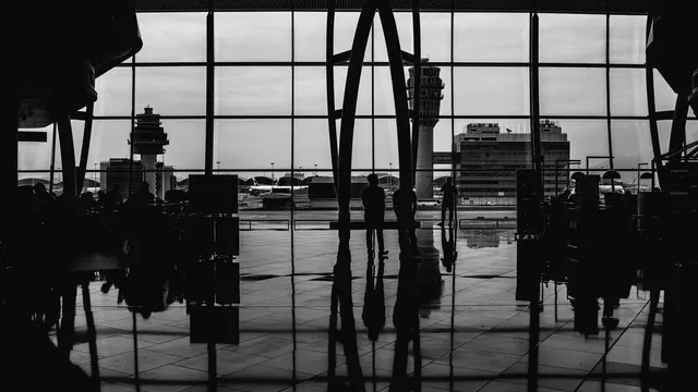 Reisende vor einer Fensterfront im Terminal in Schwarz-Weiß – Orientierung im Terminal am Flughafen Stuttgart
